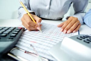 Mulher com um lápis e uma calculadora fazendo cálculos enquanto estuda sobre o código tributário municipal de seu município em um artigo da Sticorp